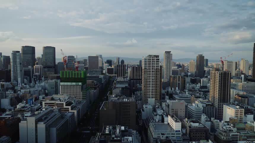 City buildings and skyscrapers and two construction cranes under a cloudy blue sky as mountains sit in the distance