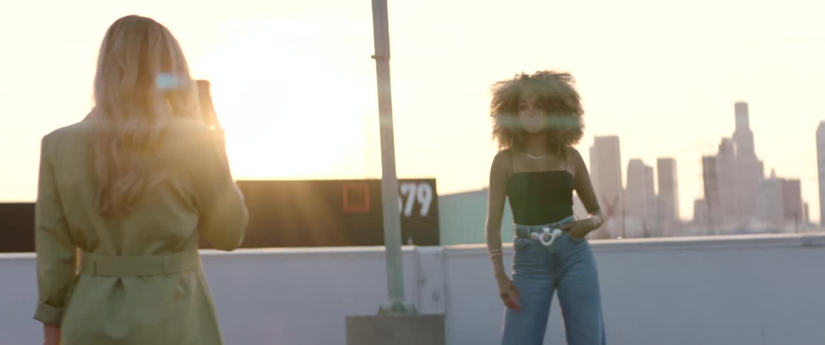 Young woman modeling on the roof of a building next to the city skyline at sunset