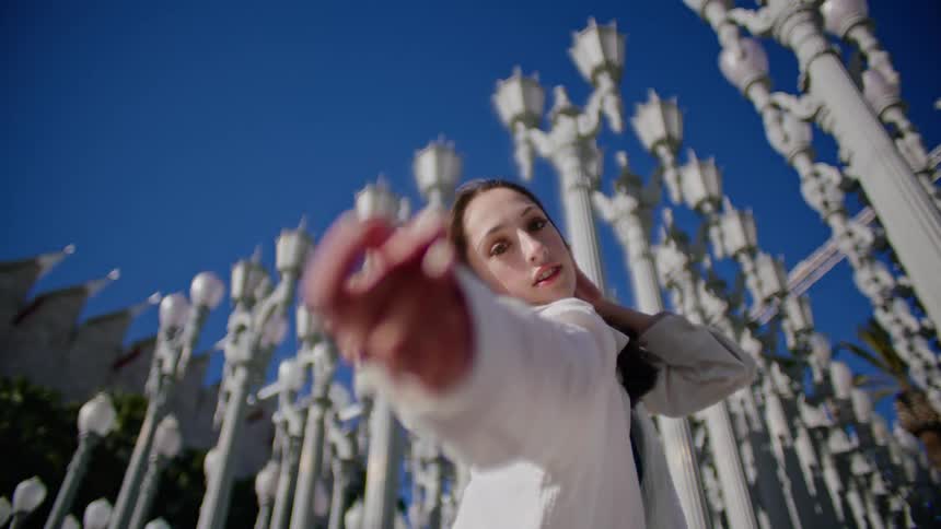 Young woman slowly dancing in front of streetlamp on a park in the city
