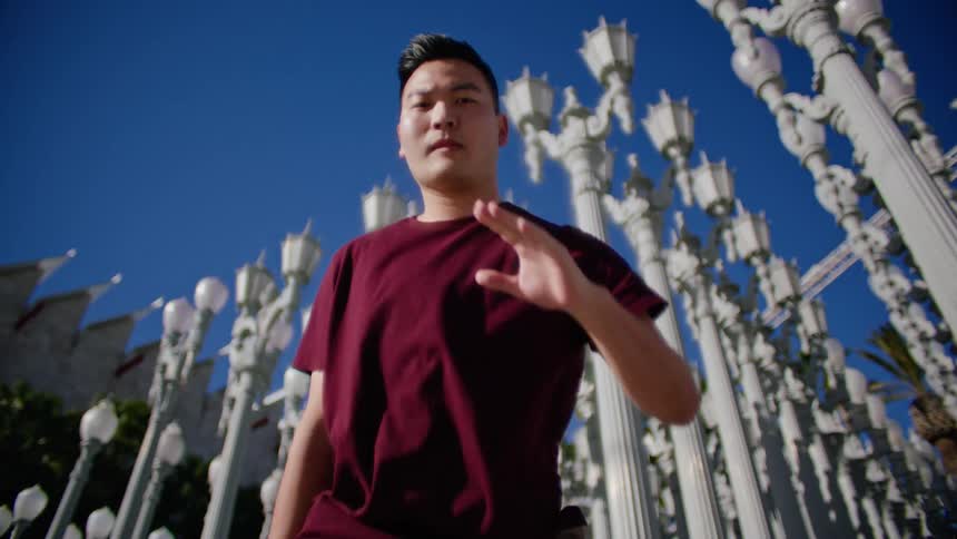 An asian male performs a series of dance moves outdoors in front of a multitude of lamp posts