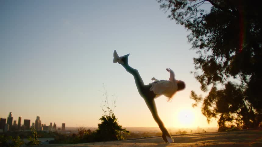 A woman kicks her leg high above her head with the city skyline behind her