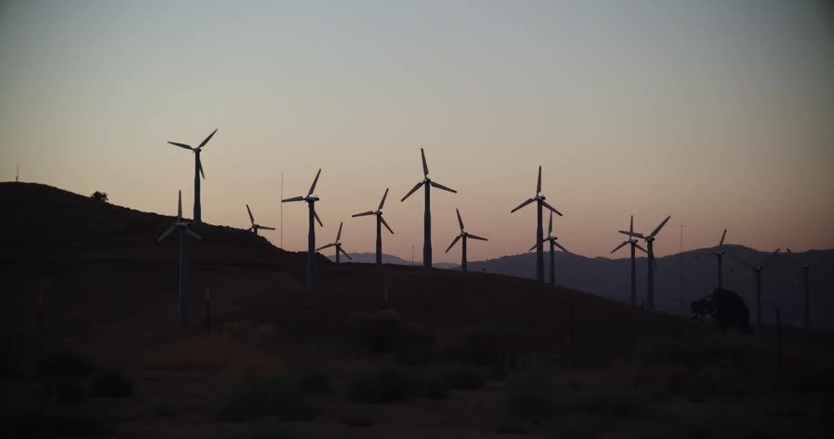 Turbines on a wind farm spinning on a hillside at sunrise