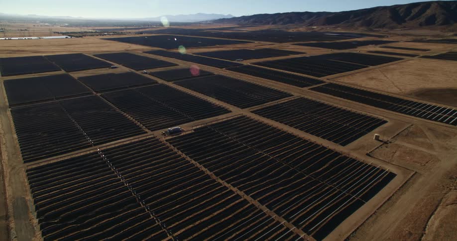 The sun shines on solar panels on a solar farm surrounded by mountains
