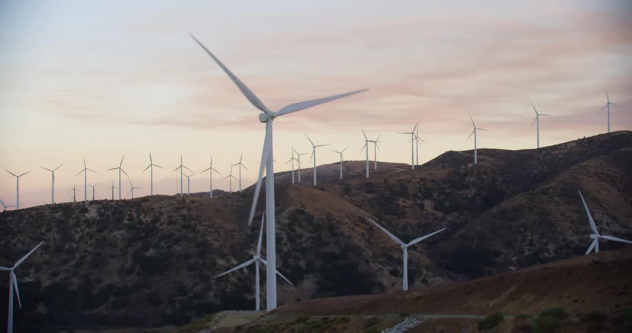 Wind turbine farm spinning on a hillside at dusk in the countryside
