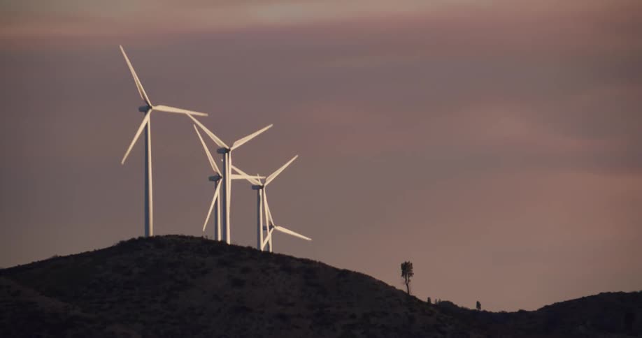 White wind turbines spin on top of a hill under a cloudy sky