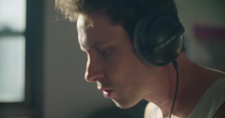 Young man wearing headphones playing drums in the living room at home in the morning