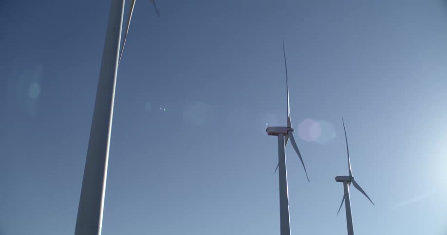 Blades of the wind turbines spin under a sunny blue sky