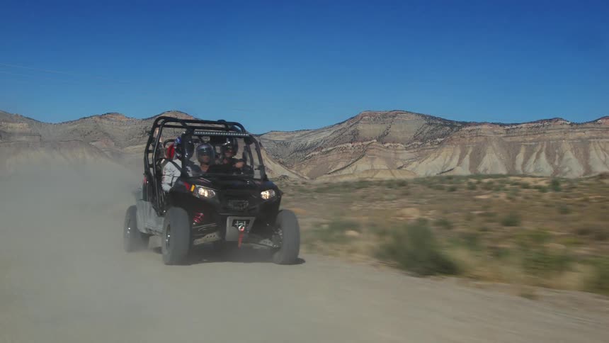 Four people riding a quad all terrain buggy vehicle kicking dust on a dirt road in the badlands
