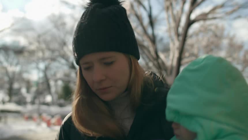 Worried mother wearing winter clothes walking down the street and carrying her baby wearing a green baby jacket during the day
