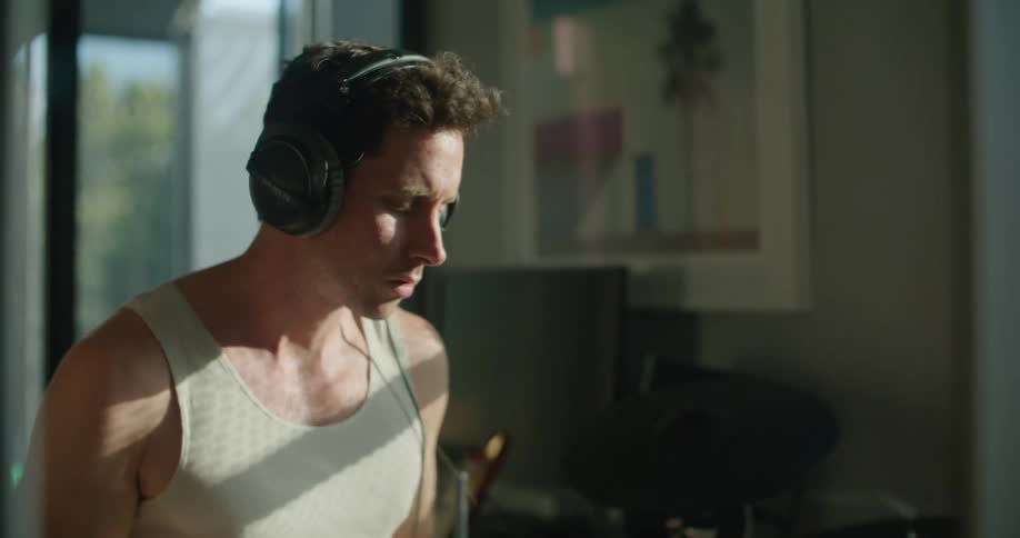 Young man wearing headphones playing drums in the living room at home in the morning