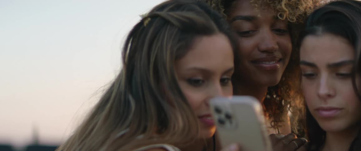 Group of young female friends looking at a phone smiling and talking outdoors at sunset