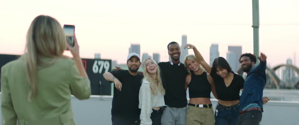 Group of friends standing together smiling and posing for a picture a woman is taking with a smartphone