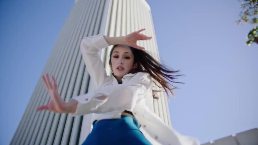 Young woman energetically dancing in front of a white skyscraper in the city