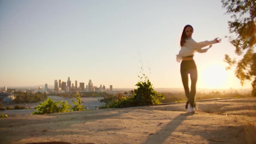 White woman dancing outdoors with the view of a big city in the background during sunset