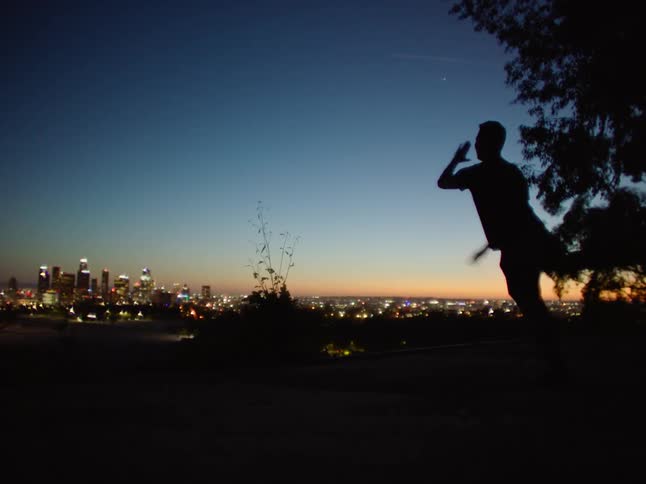 Silhouette of a man dancing in front of the city skyline at evening