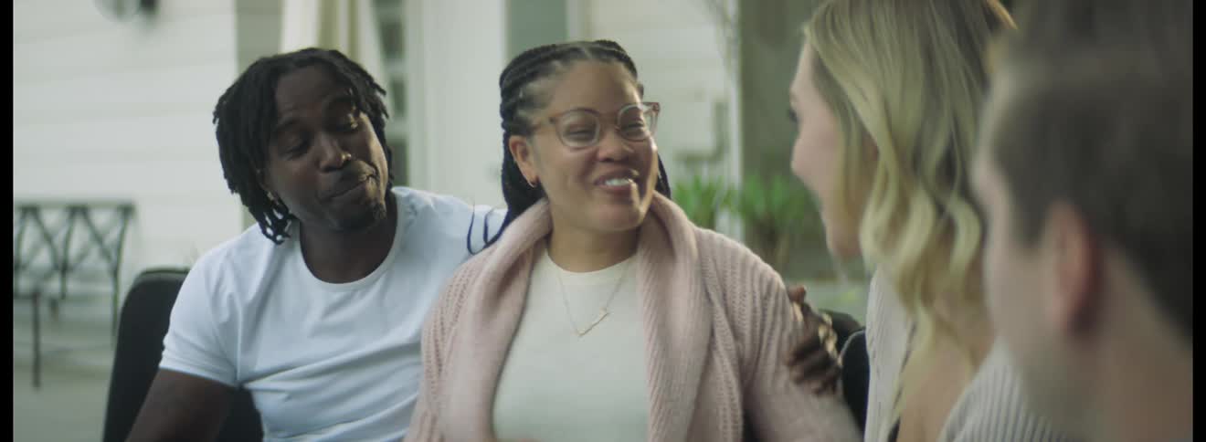A man rubs his wifes shoulder as they sit and talk and laugh with another couple and then the two men high five one another
