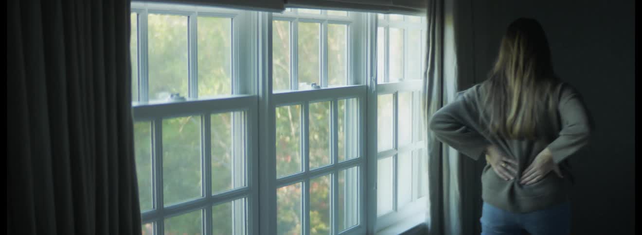 Pregnant woman walks back and forth near window rubbing her belly and her back