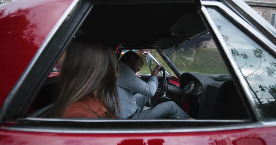 A man climbs into the drivers seat of a vintage car while his girlfriend waits