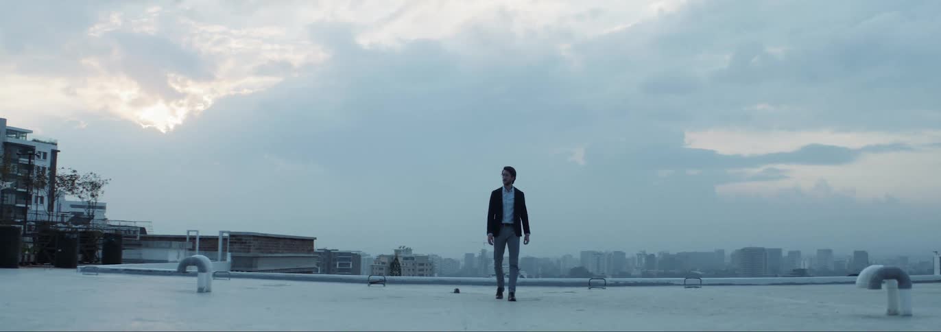 Man wearing formal clothes walking on the roof top of a building in the middle of big city on a cloudy day