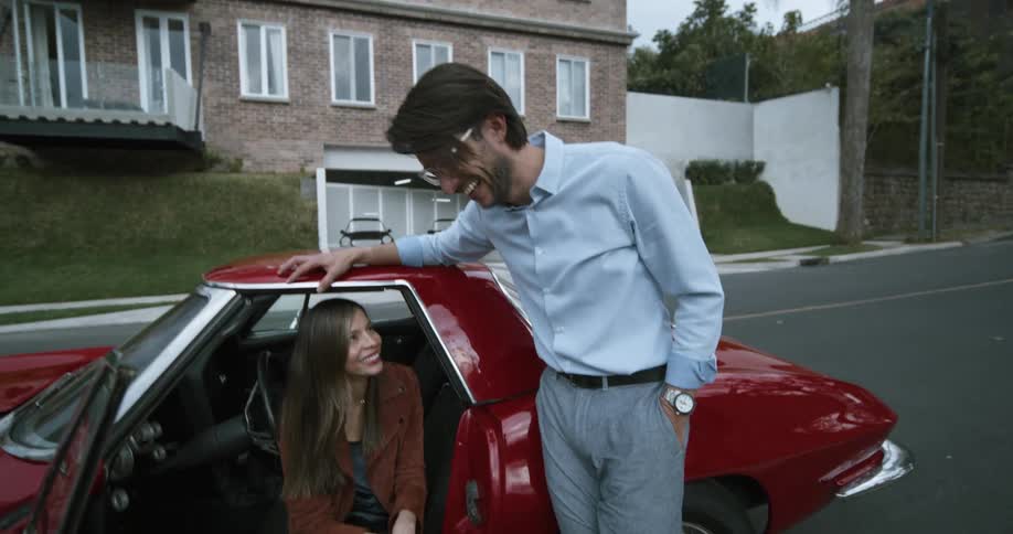 A man and woman laugh by the car