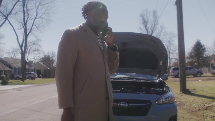 A man talks on his cell by his broken down car