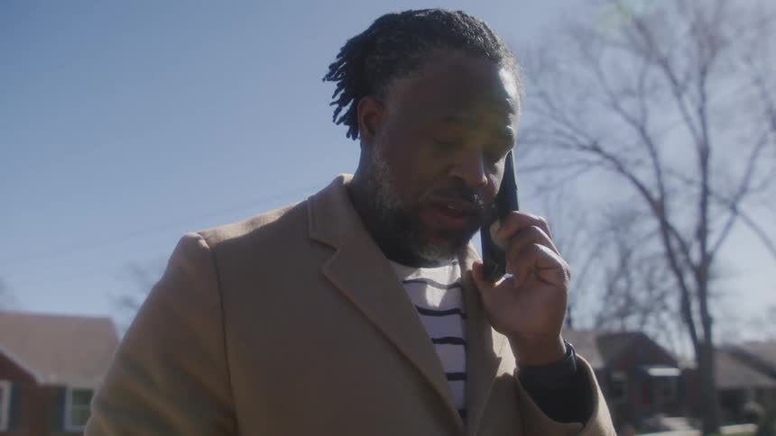A man talks on the phone standing in the street in front of his broken down car