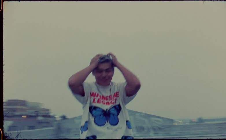 A teenage boy on a rooftop puts his hands on his head and jumps and spins in a circle