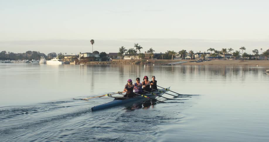 Crew of women rowing on a kayak in the calm surface of a lake near a marina at morning