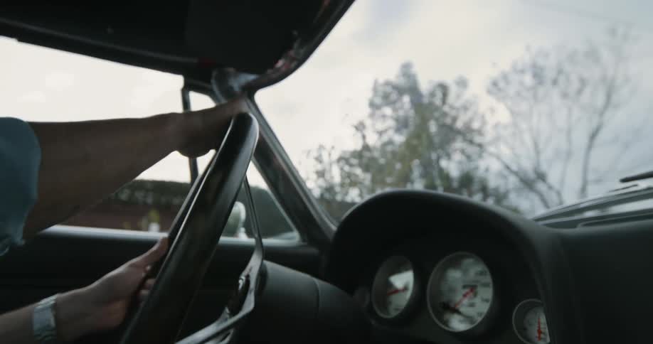 Hands of a man steering the wheel and driving a car through a residential neighborhood