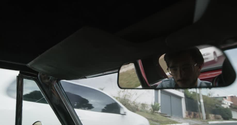 Face of a man driving a car on a neighbrohood reflected on the rearview mirror