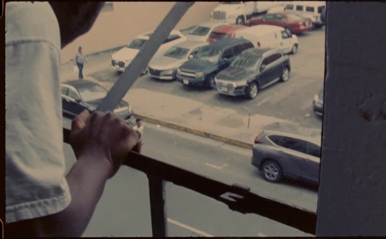 Man leans out window to watch skateboarder riding board down street