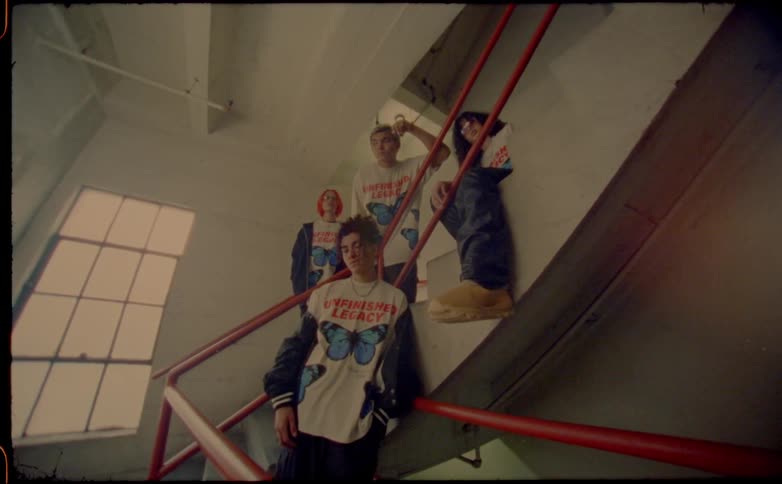 Group of teenagers wearing the same shirt sitting and standing around a building staircase caught on vintage film