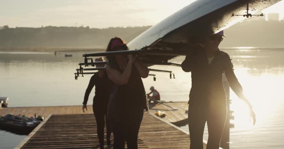 Women carrying a rowboat over a wooden pier in a lake at morning