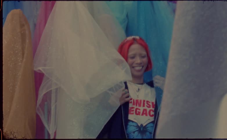 Young teenage woman with pink hair reclined on a wall covered with colorful cloths