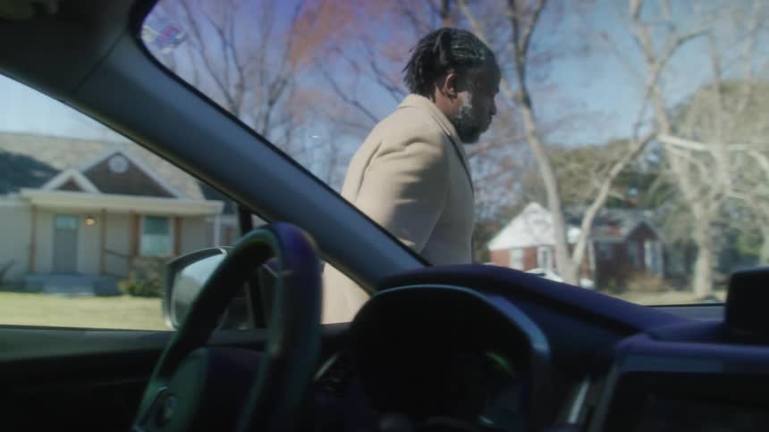 Man gets out of car and walks around to lift car hood as he shakes his head