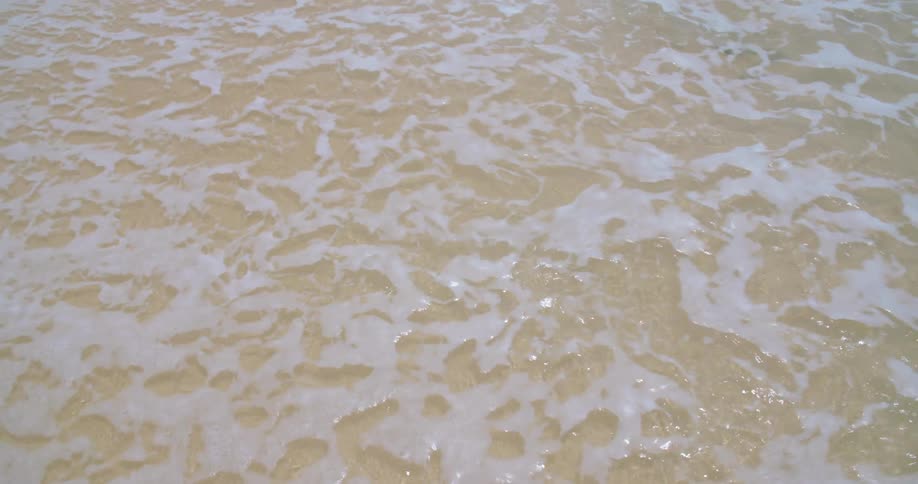Foamy ocean waves break against sand beach