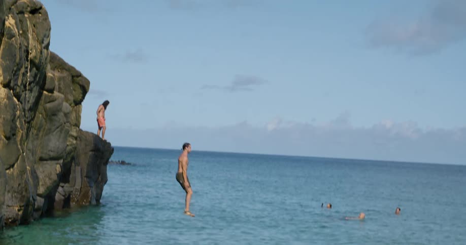 Man with brown shorts jumps off cliff into ocean water