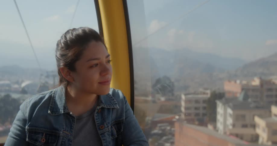 Woman rides in overhead cable car looking out at town and smiling on foggy day