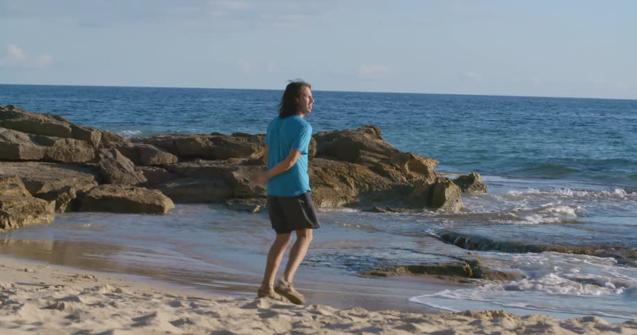Young man near the water on a beach catches a frisbee and throws it back