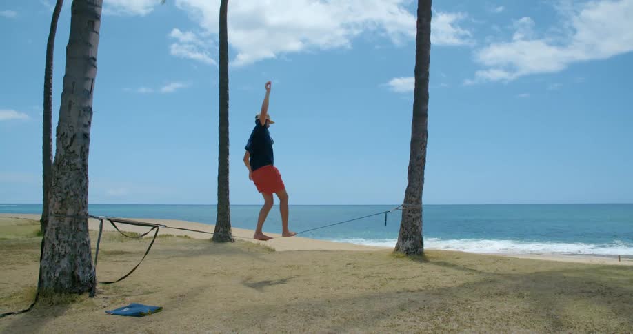 A man on a beach walks across a tight rope