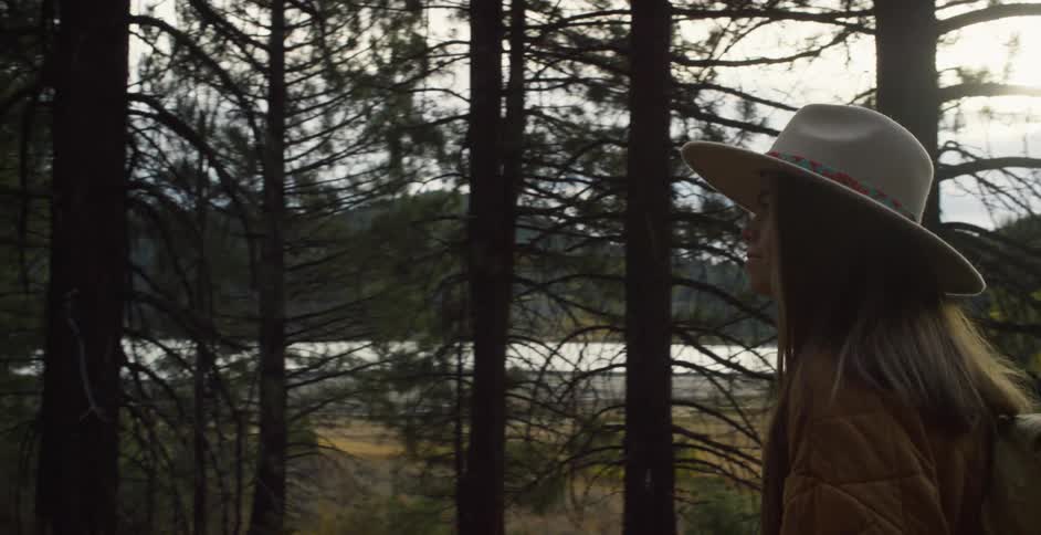 Woman with brown hat long hair jacket backpack and jeans walks on forest road in the woods