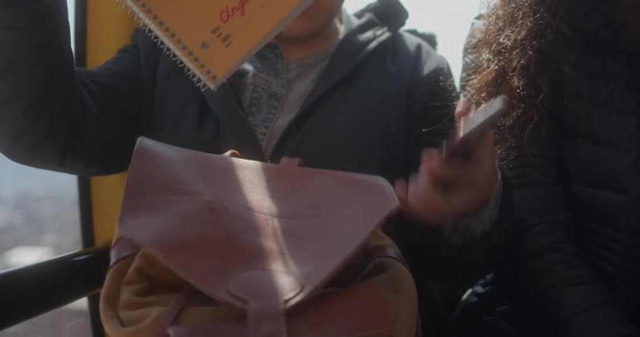 Girl sitting on a moving cable car takes a yellow notebook out of her purse