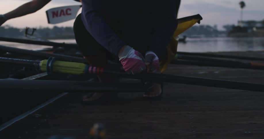 Woman kneeling over a wooden pier bolts oars on a kayak in the morning