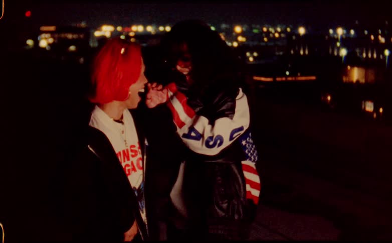 Two girl friends cover their mouths as they laugh together overlooking city lights at night