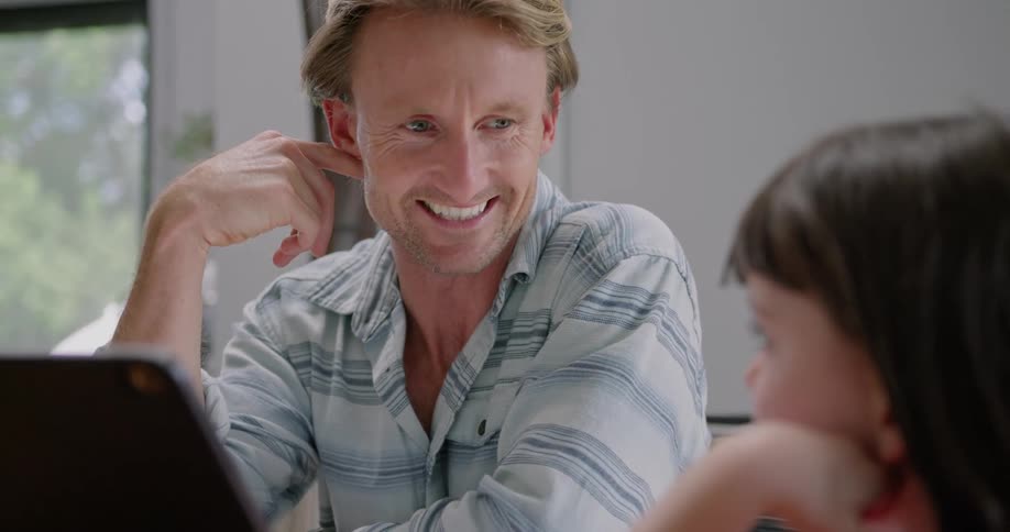 A man and his daughter laugh while looking at a laptop together