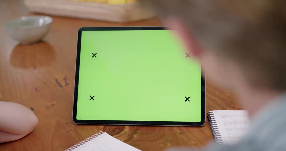 Blonde man with blue shirt sits at coffee table using tablet next to notebooks