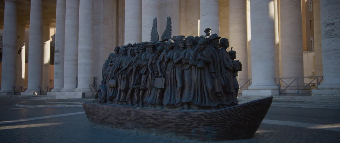 Large sculpture of refugees crowded on boat stands near building with large columns
