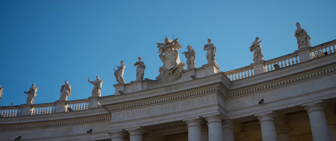 Sculptures of men line the rooftop of a columned building