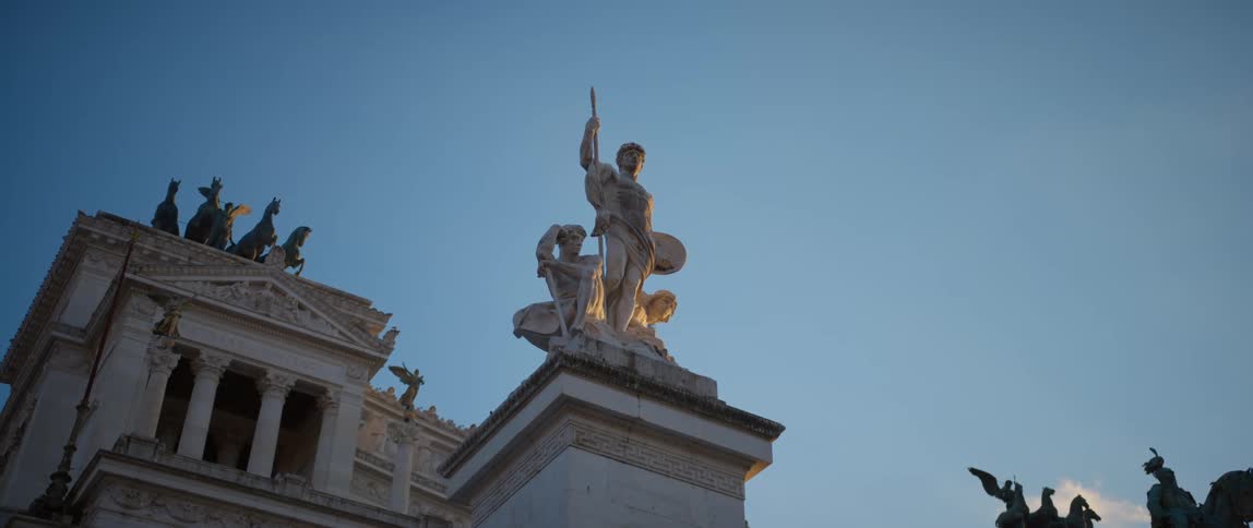 A bird flies above statues and sculptures on columns at the vittoriano in rome