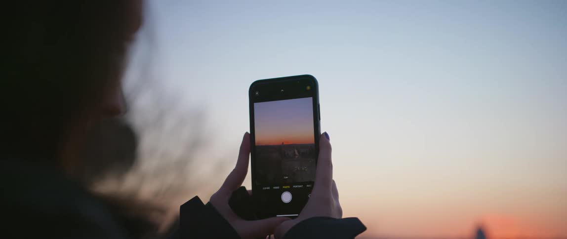 A person is taking photos of the sunset with a smartphone